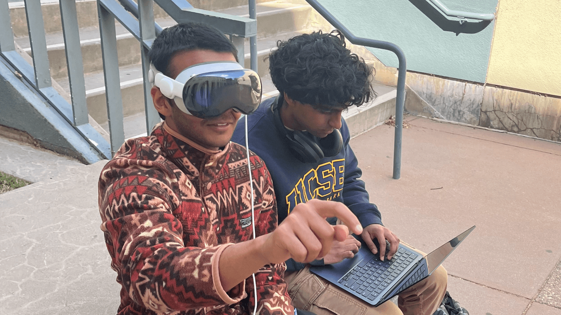 Two club members testing an Apple Vision Pro headset with a laptop on campus steps