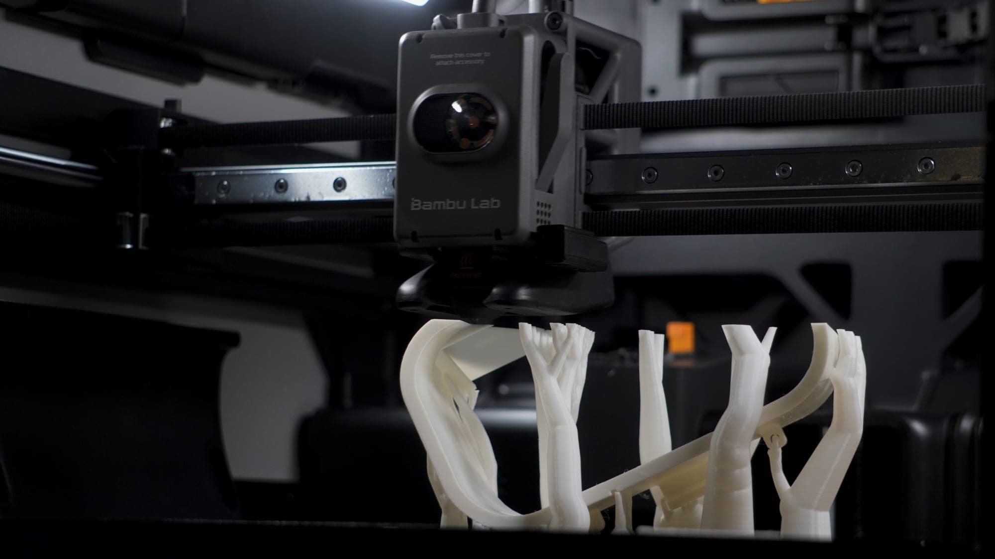 A Bambu Lab 3D printer mid-print, printing white articulated support brackets
