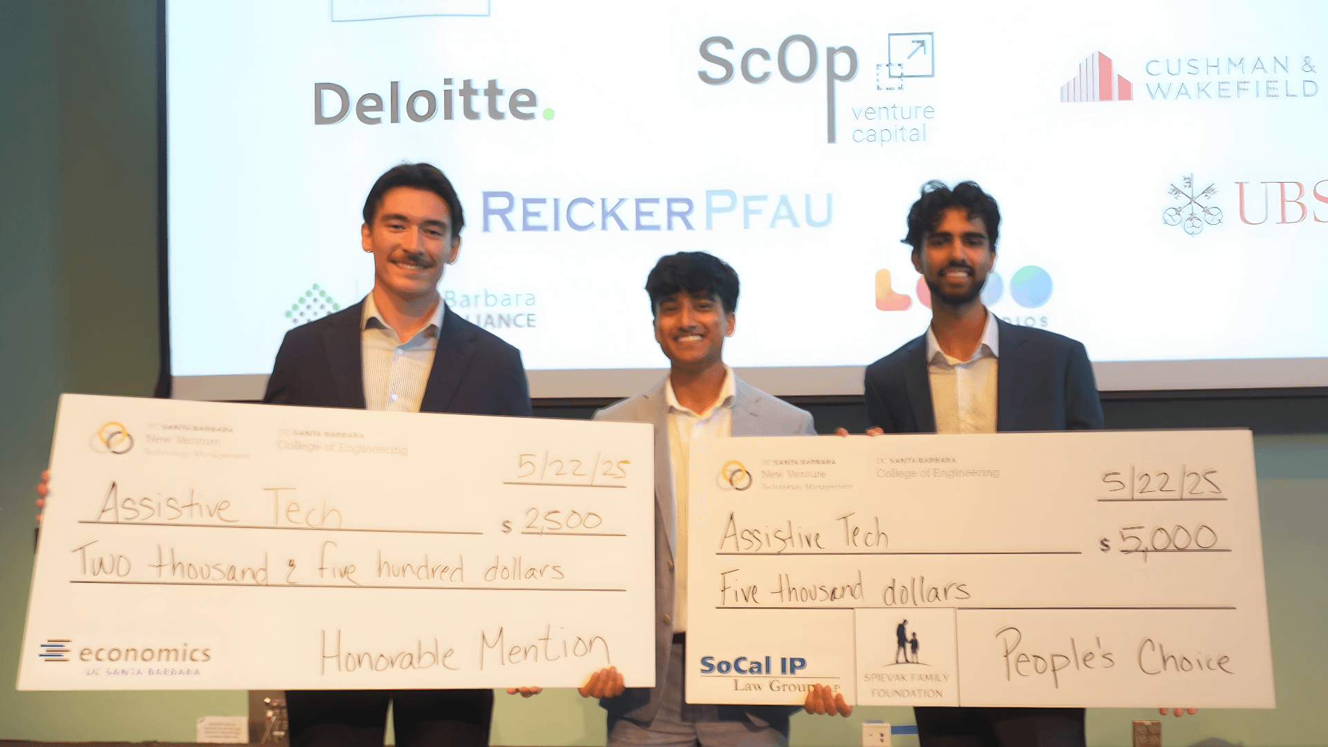Three club members accepting award checks on stage at the UCSB New Venture Competition, sponsor logos behind them